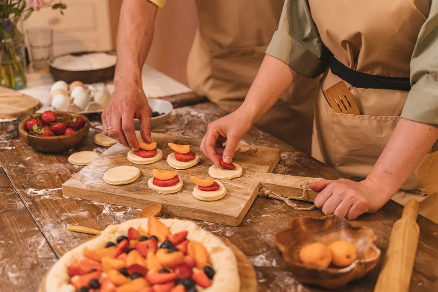 Mani che decorano le crostatine con la frutta sul tavolo di legno