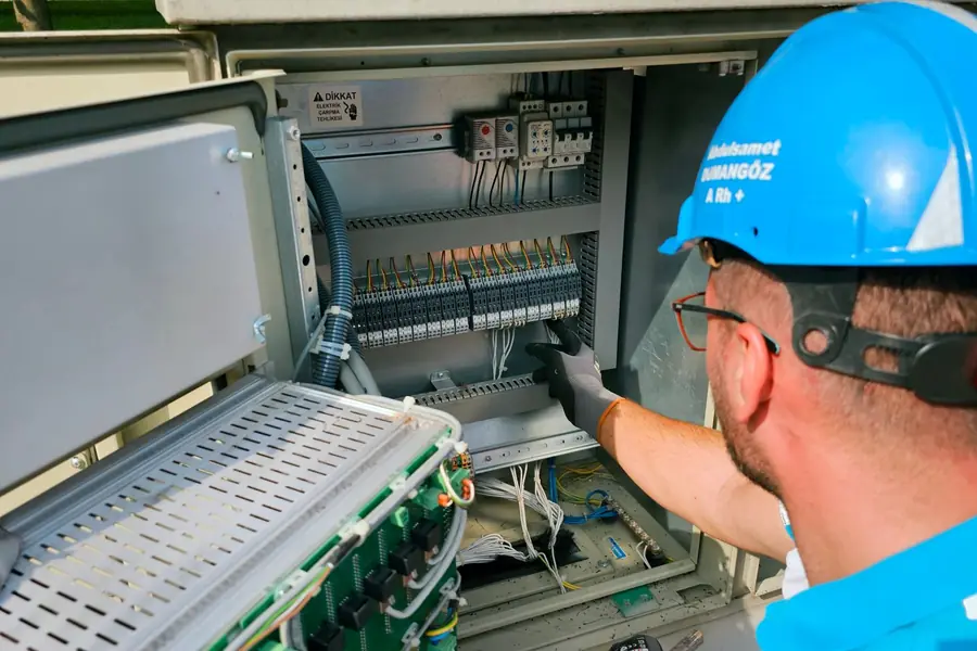 Elettricista con il casco al lavoro su un quadro all'aperto