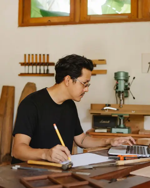 Un artisan à son établi prend des notes à côté d’un ordinateur portable