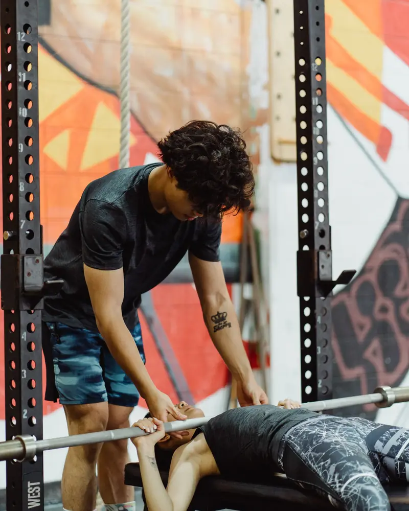 Personal trainer che assiste un cliente alla panca in palestra