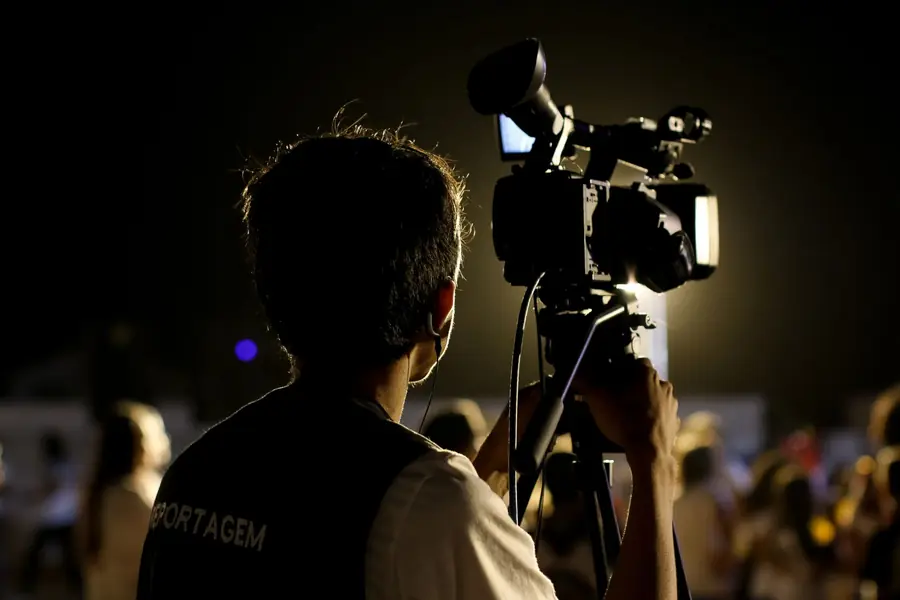 Operatore che filma un evento di sera con la videocamera sul cavalletto